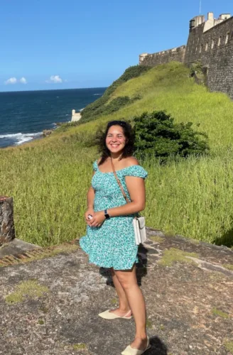 The author Izzie standing in front of the ocean in Old San Juan, Puerto Rico, with the old fort in the background. 